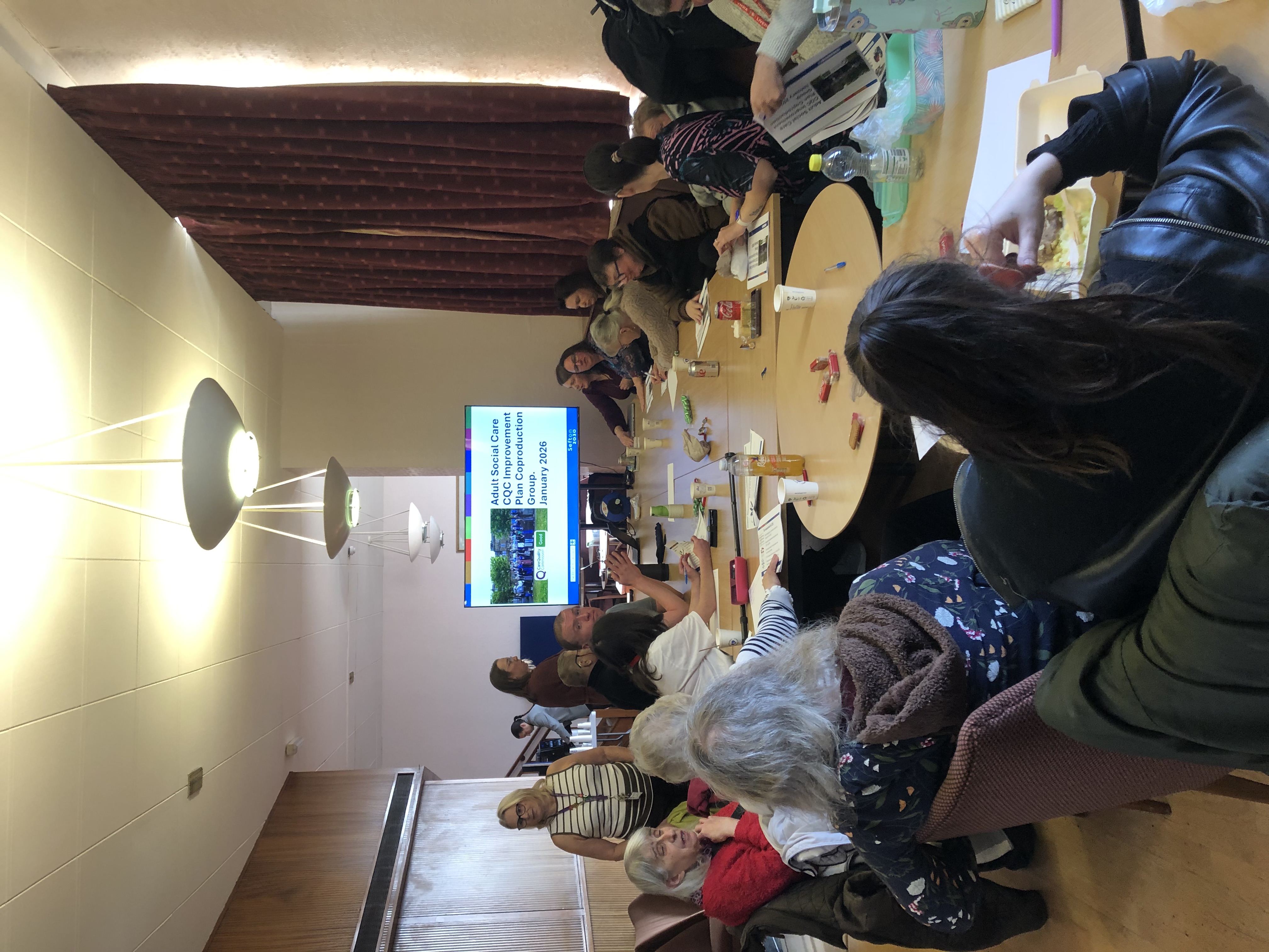 Photograph taken at the first meetin in January 2026 showing the Bar Lounge in Bootle Town Hall with a presentation screen being shown to a group of 30 people who attended